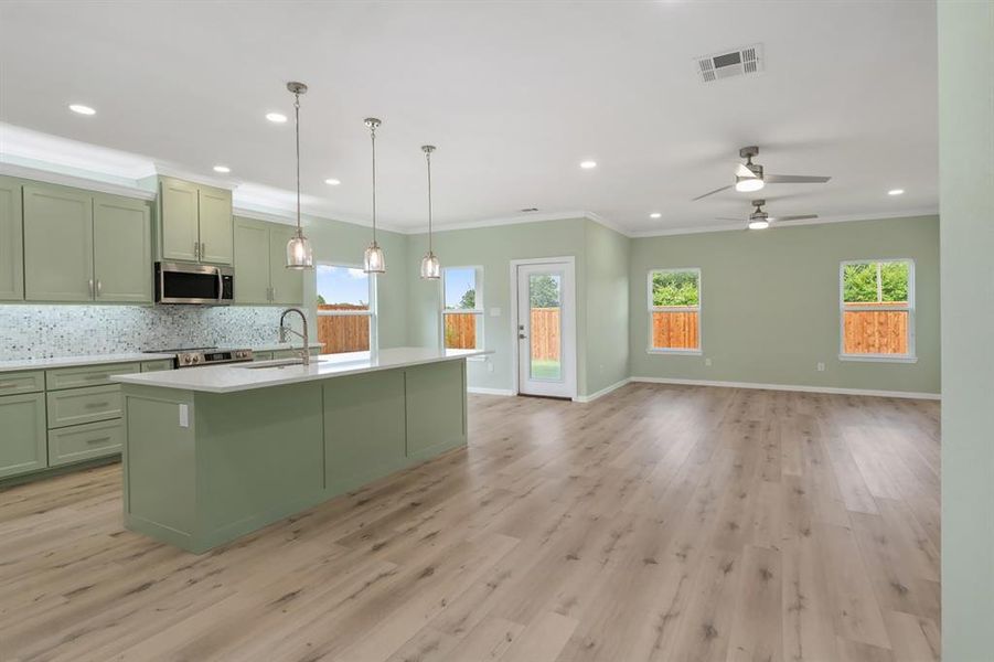 Kitchen with light hardwood / wood-style floors, appliances with stainless steel finishes, a healthy amount of sunlight, and an island with sink