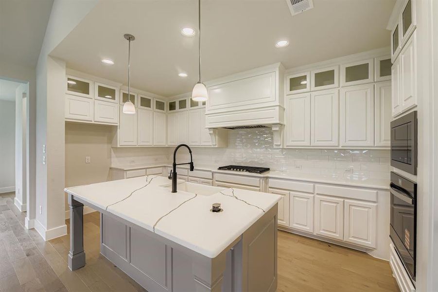 Kitchen with tasteful backsplash, light wood-type flooring, a center island with sink, recessed lighting, and white cabinetry