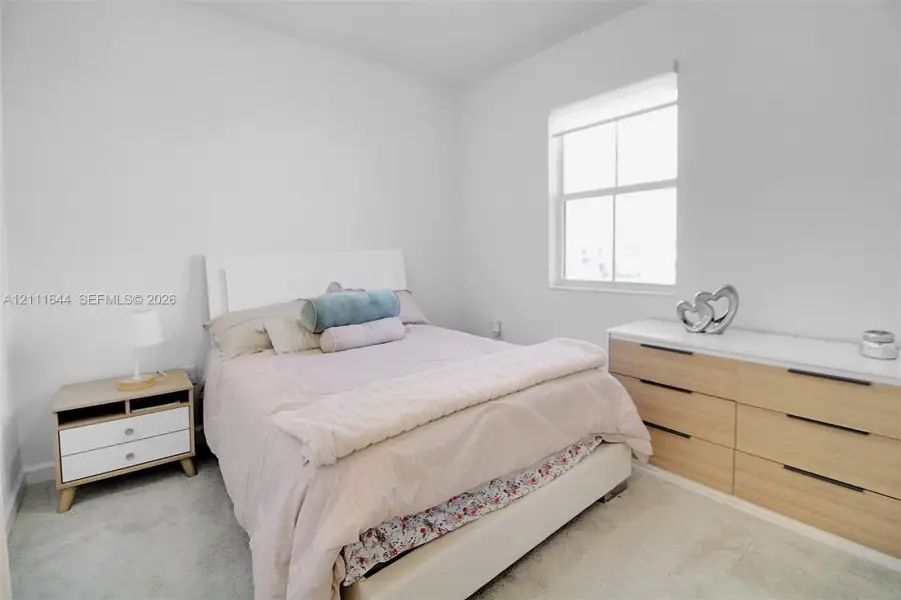 Neutral-toned interior space featuring light-colored wall-to-wall carpeting and a single-pane window with a roller shade Neutral-toned interior space featuring light-colored wall-to-wall carpeting and a single-pane window with a roller shade
