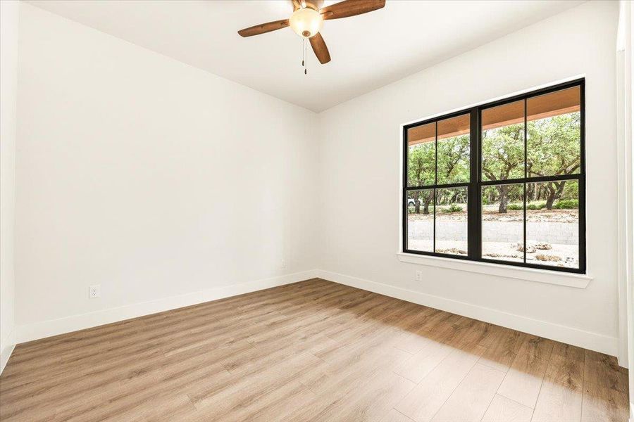 A well-lit room features light wood flooring and a refreshing view of lush trees through a large window.