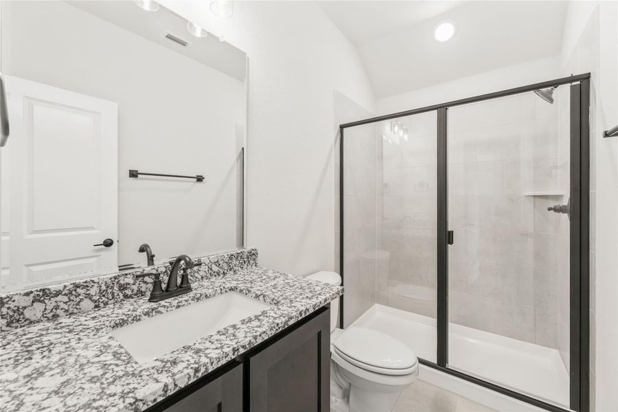 Bathroom with granite vanity, dark cabinets, glass-enclosed shower, and white toilet against white walls Bathroom with granite vanity, dark cabinets, glass-enclosed shower, and white toilet against white walls