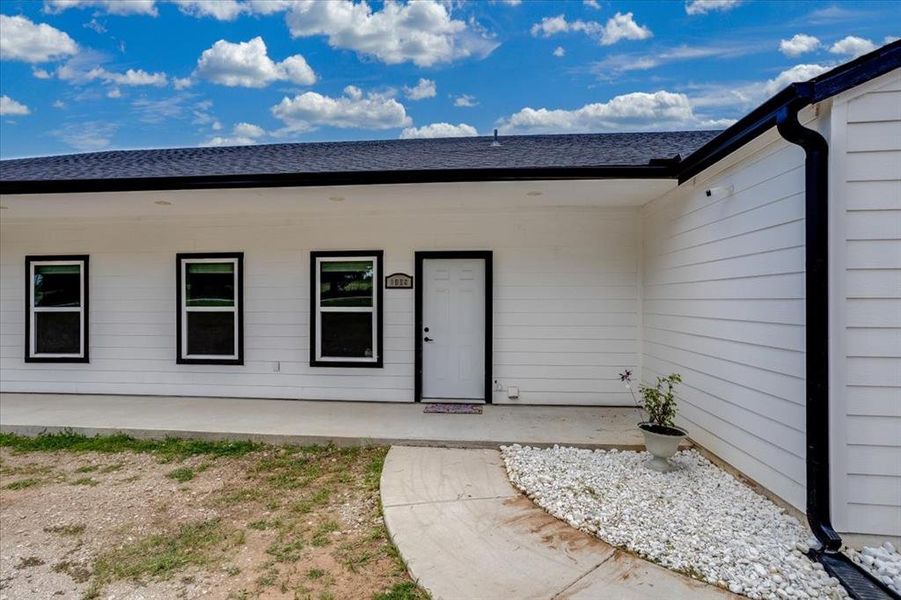 White horizontal siding exterior with black trim windows, a dark shingle roof, and a concrete pathway leading to the front entry