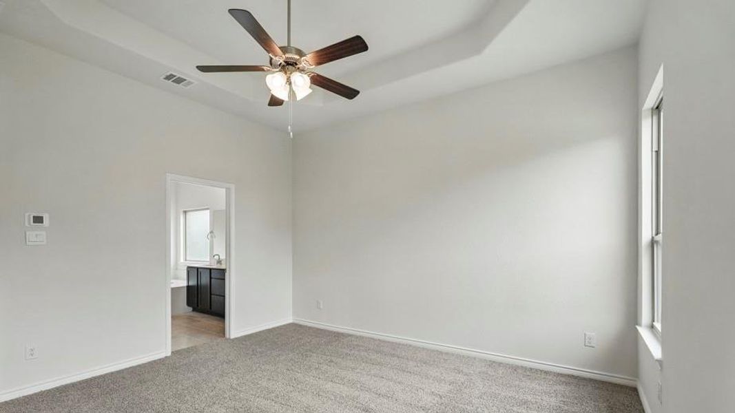 Spacious room featuring gray carpeting, a tray ceiling, and a ceiling fan with integrated lighting