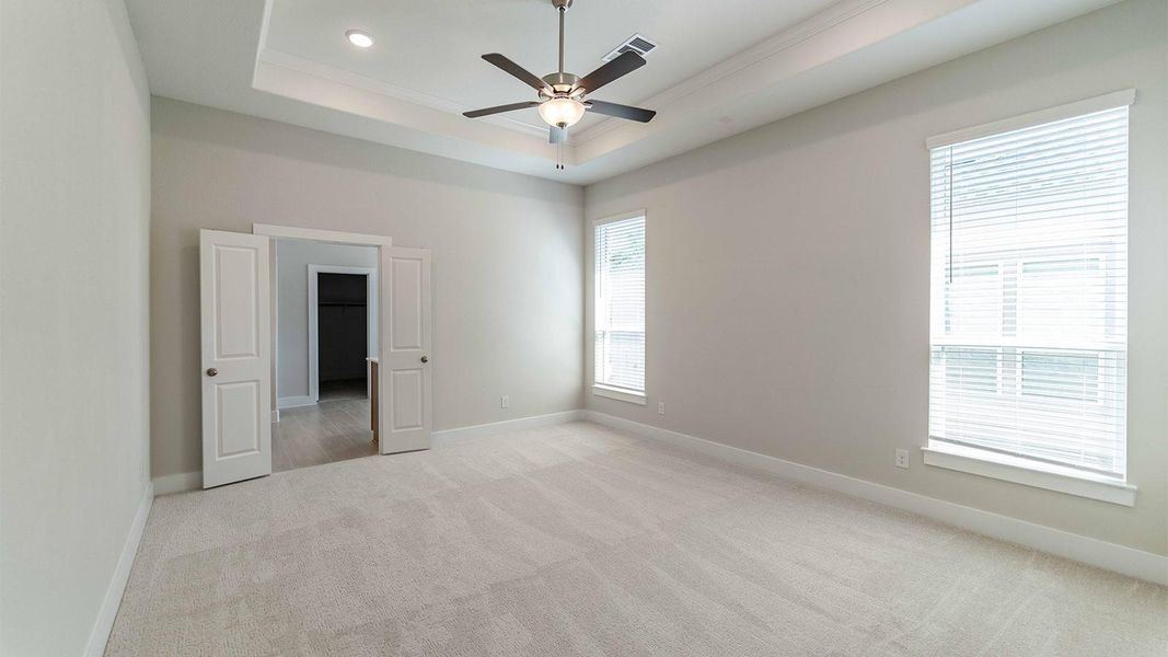 Unfurnished bedroom featuring light colored carpet, a raised ceiling, a ceiling fan, ornamental molding, and recessed lighting Unfurnished bedroom featuring light colored carpet, a raised ceiling, a ceiling fan, ornamental molding, and recessed lighting