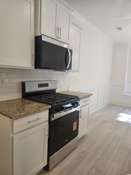 Kitchen with stainless steel appliances, wainscoting, dark stone countertops, white cabinets, and crown molding Kitchen with stainless steel appliances, wainscoting, dark stone countertops, white cabinets, and crown molding