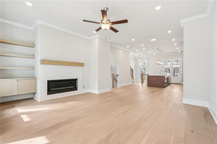 Unfurnished living room featuring recessed lighting, ornamental molding, a glass covered fireplace, a ceiling fan, and light wood-type flooring