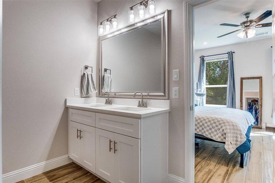 Ensuite bathroom featuring wood finish floors, double vanity, ceiling fan, and a textured wall