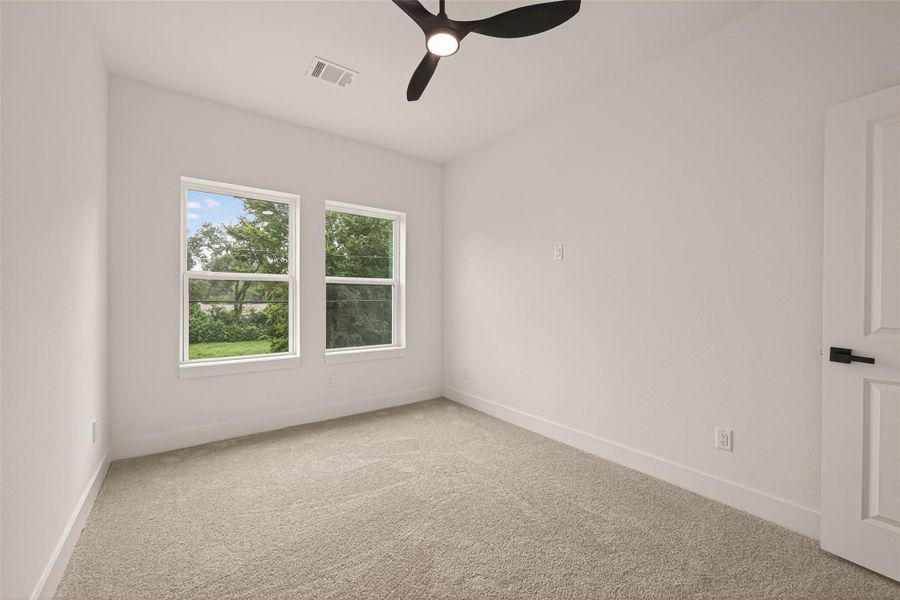 This is a bright, cozy room with two large windows offering a view of lush greenery. It features clean, neutral walls, a modern ceiling fan, and soft carpet flooring, creating a welcoming atmosphere. This is a bright, cozy room with two large windows offering a view of lush greenery. It features clean, neutral walls, a modern ceiling fan, and soft carpet flooring, creating a welcoming atmosphere.