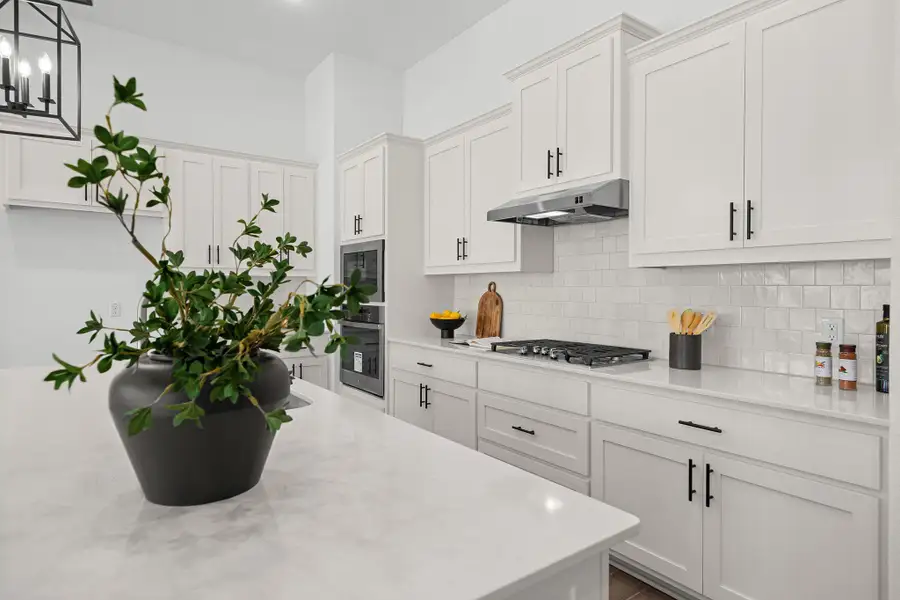 Kitchen with backsplash, white cabinetry, light stone counters, and hanging light fixtures