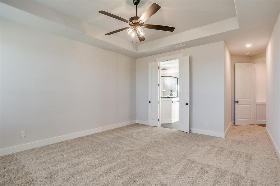 Empty room with a raised ceiling, ceiling fan, and light carpet