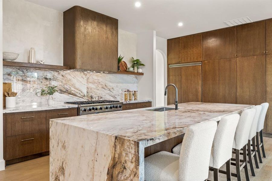 Kitchen with open shelves, light stone counters, a breakfast bar area, backsplash, and light wood finished floors Kitchen with open shelves, light stone counters, a breakfast bar area, backsplash, and light wood finished floors