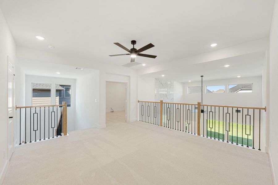 Open upstairs loft with carpet, ceiling fan, and metal stair railings with wood posts