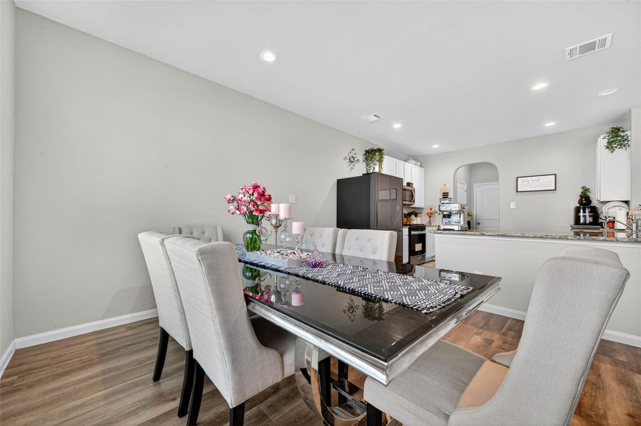 This photo showcases a modern dining area connected to a kitchen. The space features a sleek dining table with upholstered chairs and a decorative centerpiece. The kitchen is equipped with contemporary appliances, granite countertops, and ample cabinetry, creating a seamless and inviting open layout.
