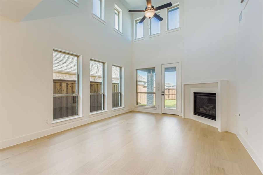 Unfurnished living room featuring light wood-type flooring, healthy amount of natural light, a ceiling fan, and a towering ceiling Unfurnished living room featuring light wood-type flooring, healthy amount of natural light, a ceiling fan, and a towering ceiling