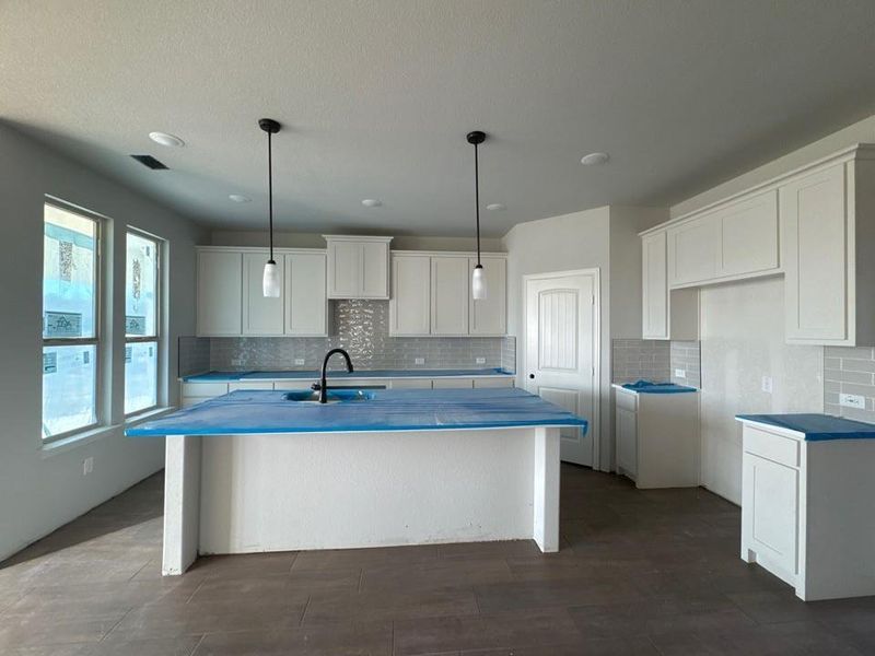 Kitchen featuring white cabinets, an island with sink, a kitchen breakfast bar, decorative light fixtures, and backsplash
