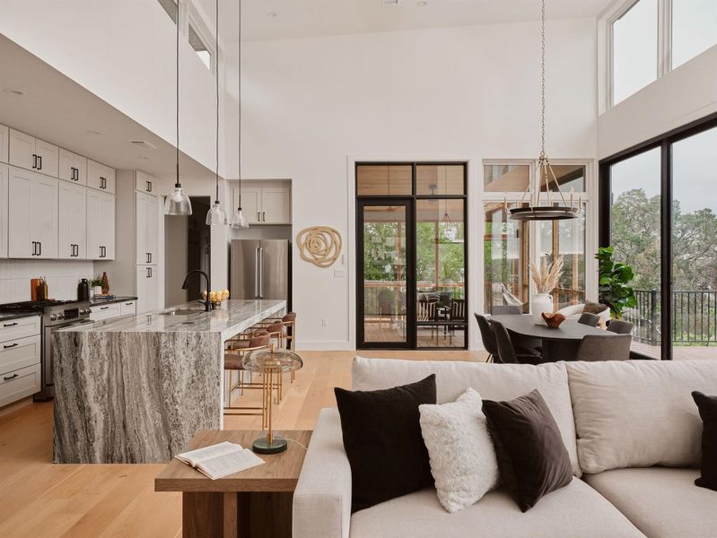 Open-concept living space with light wood-finish flooring, a kitchen featuring white cabinetry and a waterfall island, a dining area, and expansive windows