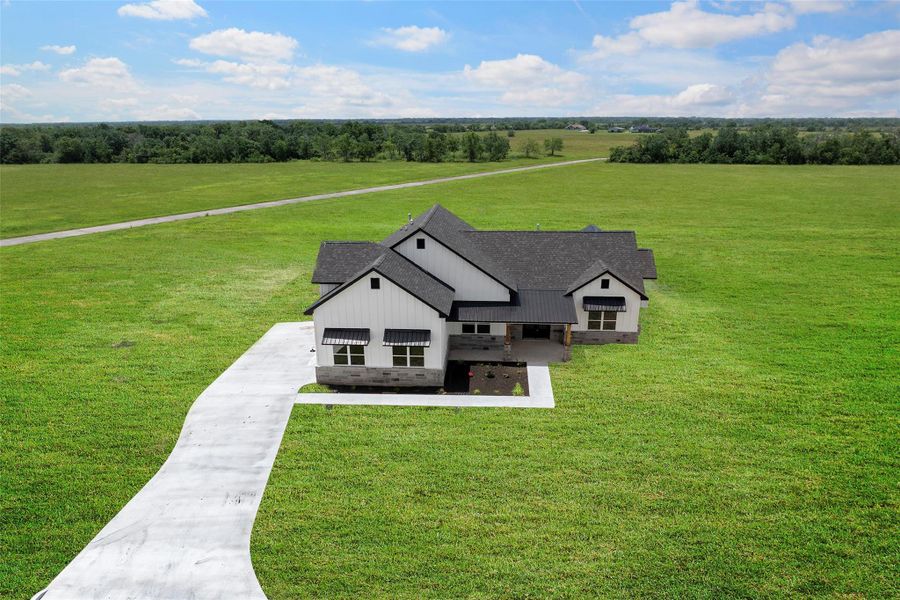 Stunning aerial view showcasing a modern farmhouse with a spacious front yard and beautiful countryside surroundings. Perfect for those seeking tranquility and style.