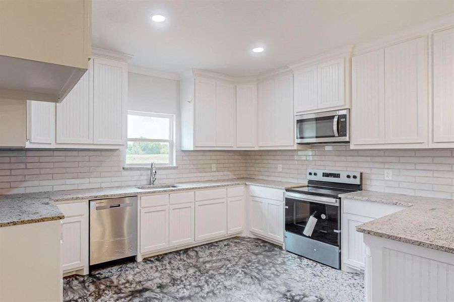 Kitchen featuring sink, stainless steel appliances, light stone counters, decorative backsplash, and white cabinets