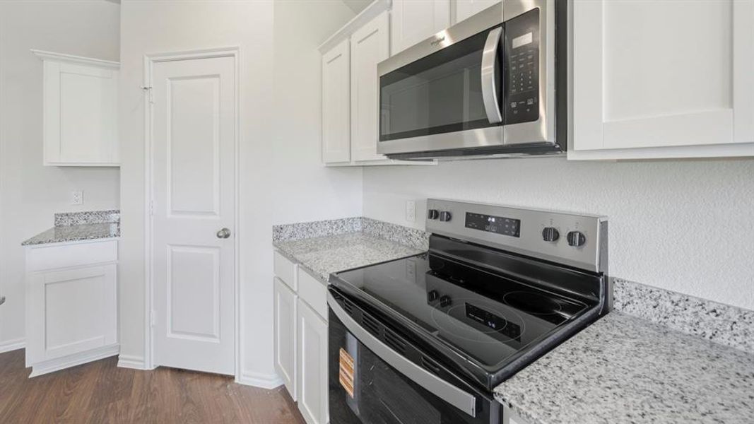 Modern kitchen featuring white cabinetry, granite countertops, wood-finish flooring, a stainless steel microwave, and a black electric range