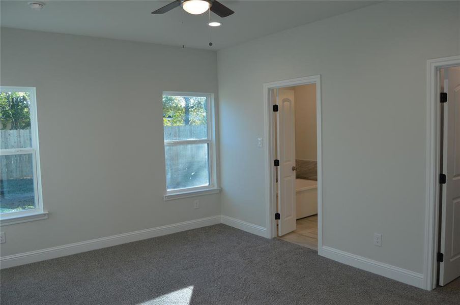 primary bedroom with ensuite bathroom, ceiling fan and multiple windows