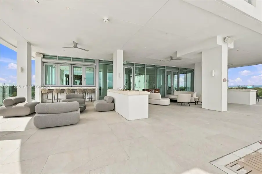 Covered terrace featuring large-format stone tile flooring, built-in stone bar counter, floor-to-ceiling glass paneling, and ceiling-mounted fans Covered terrace featuring large-format stone tile flooring, built-in stone bar counter, floor-to-ceiling glass paneling, and ceiling-mounted fans