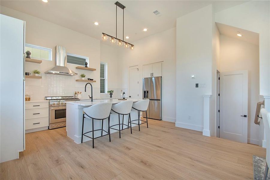 Kitchen with a kitchen bar, white cabinetry, hanging light fixtures, a towering ceiling, and island exhaust hood Kitchen with a kitchen bar, white cabinetry, hanging light fixtures, a towering ceiling, and island exhaust hood