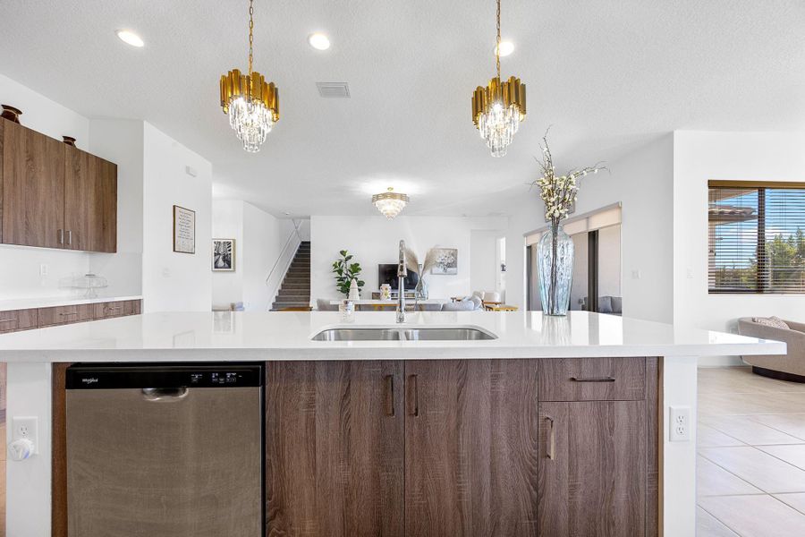 Kitchen featuring open floor plan, stainless steel dishwasher, modern cabinets, light stone counters, and a center island with sink