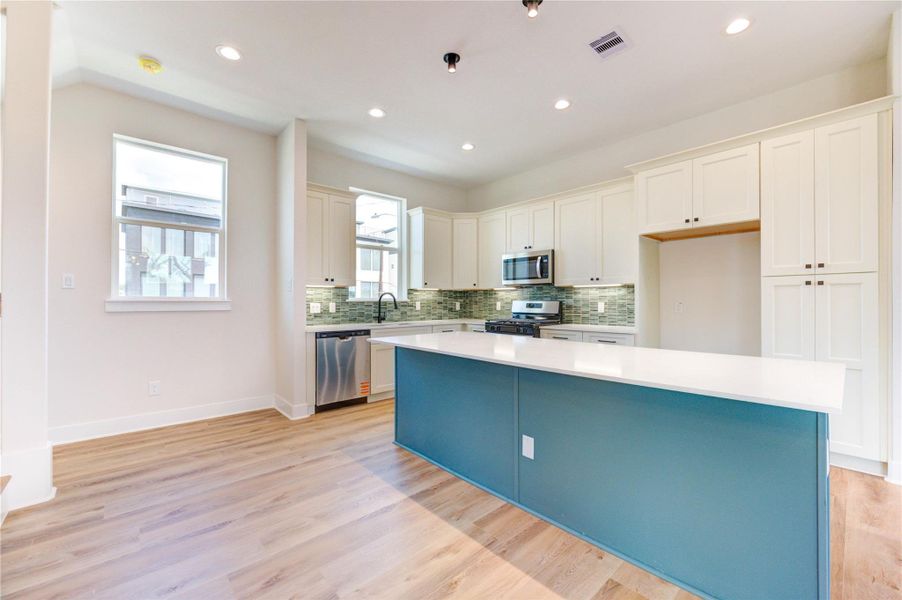 Light filled kitchen with two-tone cabinetry, quartz countertops and stainless-steel appliances. Large island with designer minimalist lighting. Light filled kitchen with two-tone cabinetry, quartz countertops and stainless-steel appliances. Large island with designer minimalist lighting.