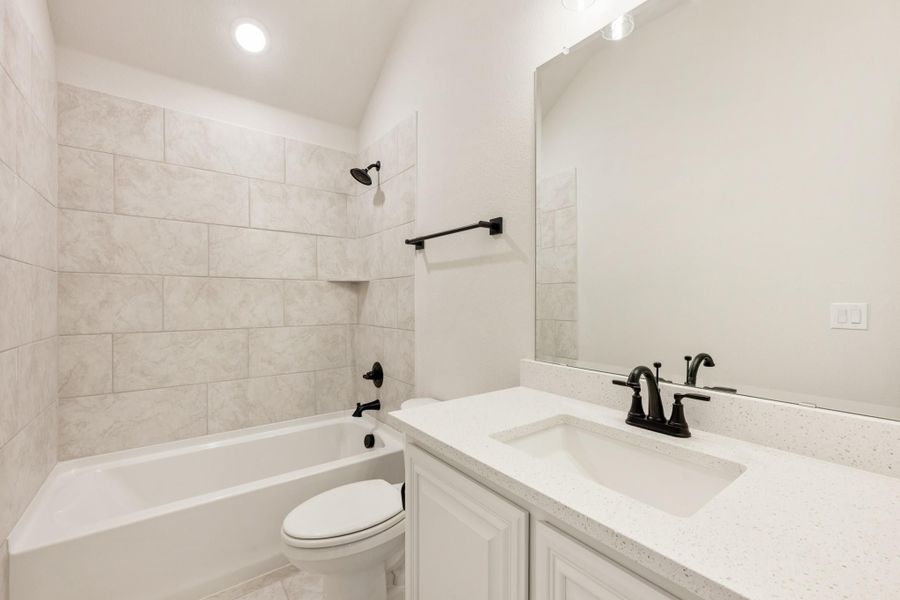 Bathroom with tiled tub-shower combo, white vanity with quartz countertop, and black fixtures