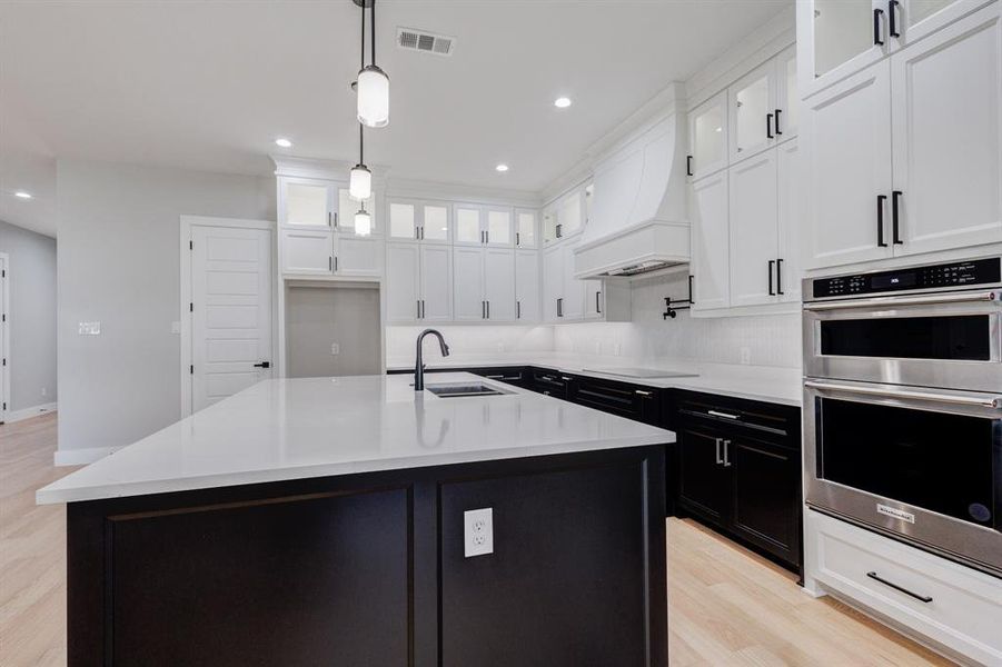 Open-concept kitchen featuring an oversized island with white countertop, black base cabinetry, and three pendant lights
