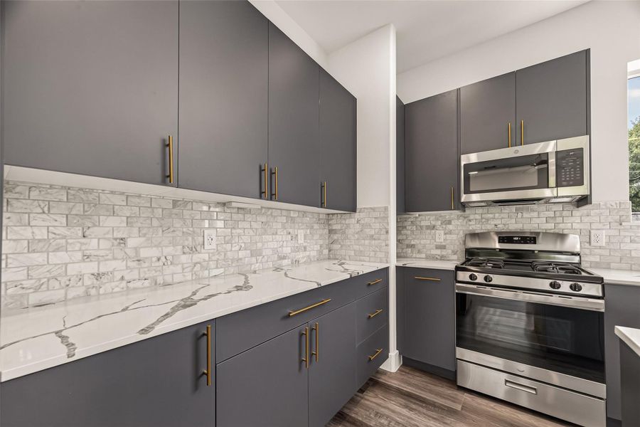 This modern kitchen features sleek gray cabinets with brass handles, a stylish marble backsplash, and stainless steel appliances. The clean lines and contemporary design create a sophisticated cooking space. This modern kitchen features sleek gray cabinets with brass handles, a stylish marble backsplash, and stainless steel appliances. The clean lines and contemporary design create a sophisticated cooking space.