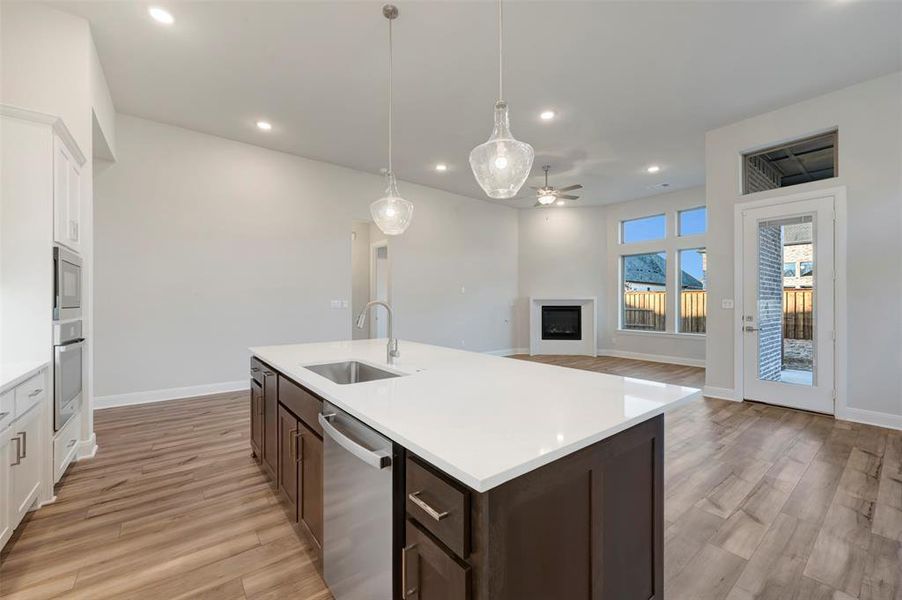 Dual tone kitchen featuring two tone cabinetry, a fireplace, pendant lighting, stainless steel appliances, and light wood-style flooring