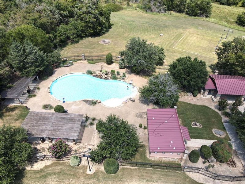 Freeform swimming pool with expansive surrounding patio, two covered pergolas, and a red metal roof structure