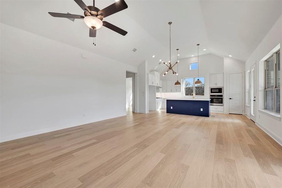 Unfurnished living room featuring light wood-style floors, a chandelier, a ceiling fan, and vaulted ceiling Unfurnished living room featuring light wood-style floors, a chandelier, a ceiling fan, and vaulted ceiling