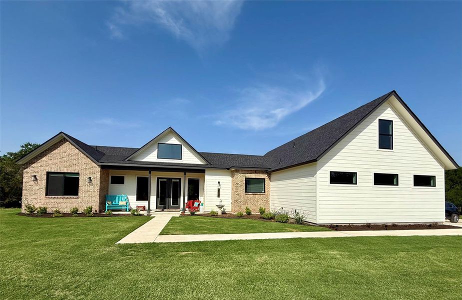 Rear view of property with brick siding, a yard, and roof with shingles