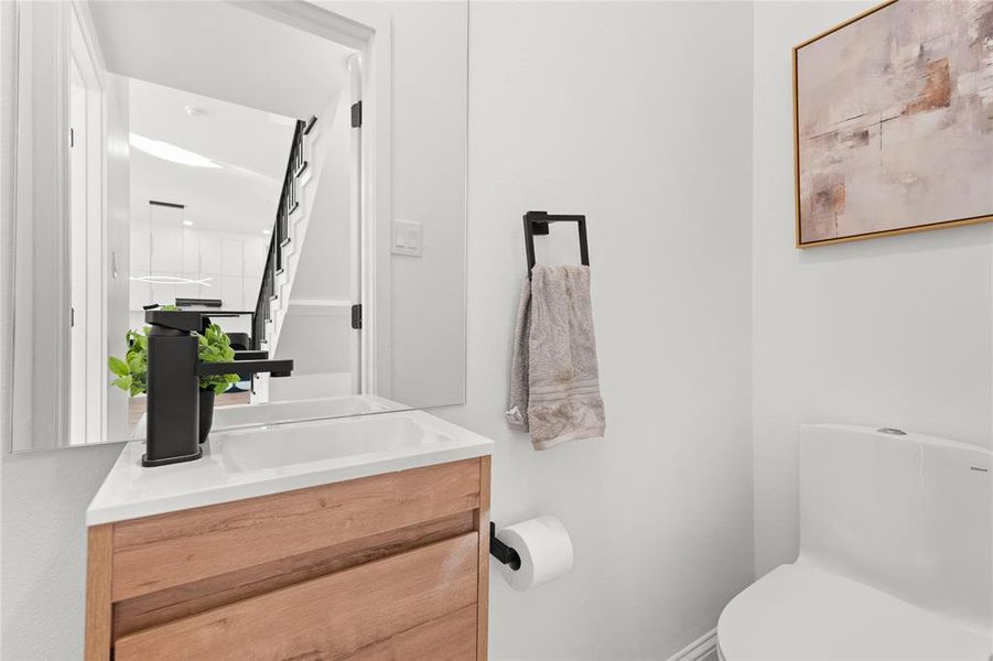 Modern powder room featuring a wood-finish vanity with an integrated sink, matte black faucet, and a clean white toilet