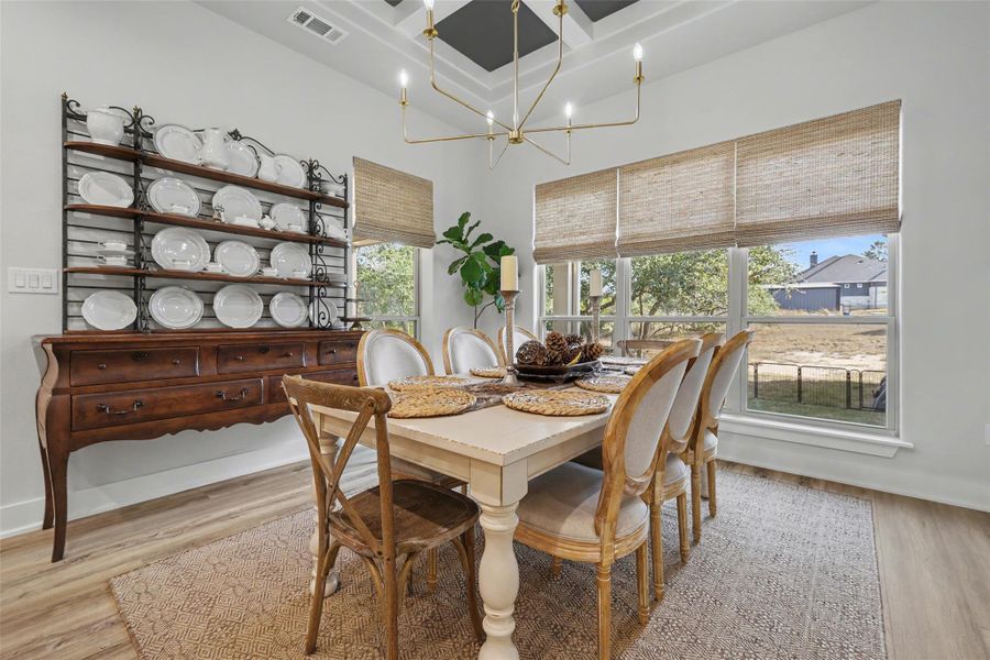 Dining room featuring coffered ceiling, light wood-style flooring, a chandelier, and a high ceiling