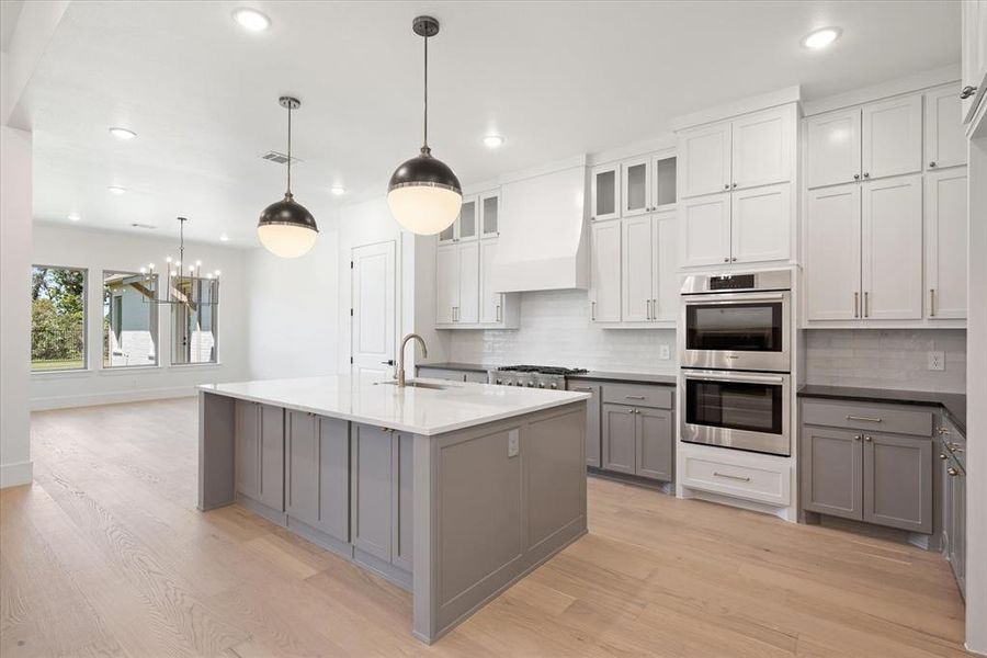 Kitchen with backsplash, light hardwood / wood-style floors, stainless steel appliances, gray cabinets, and a chandelier