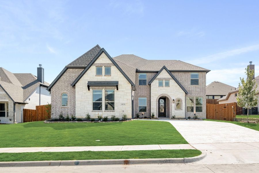 Two-story home with brick and stone exterior, arched entry, and manicured front lawn