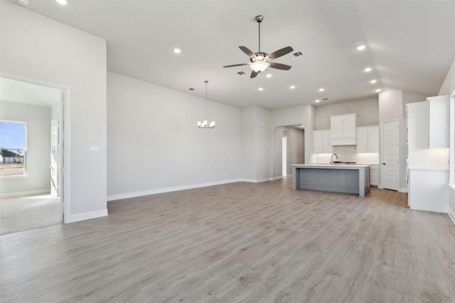 Unfurnished living room with ceiling fan with notable chandelier, light hardwood / wood-style floors, and vaulted ceiling