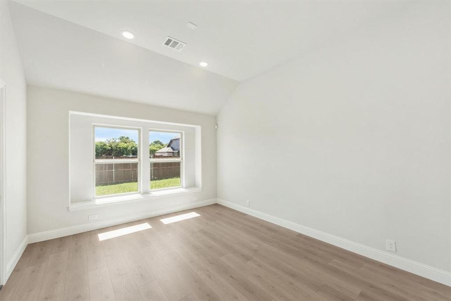Bright interior space featuring a large window, vaulted ceiling, recessed lighting, wood-finish flooring, and crisp white walls Bright interior space featuring a large window, vaulted ceiling, recessed lighting, wood-finish flooring, and crisp white walls