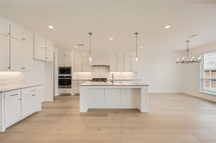 Kitchen featuring appliances with stainless steel finishes, decorative light fixtures, backsplash, and a center island with sink