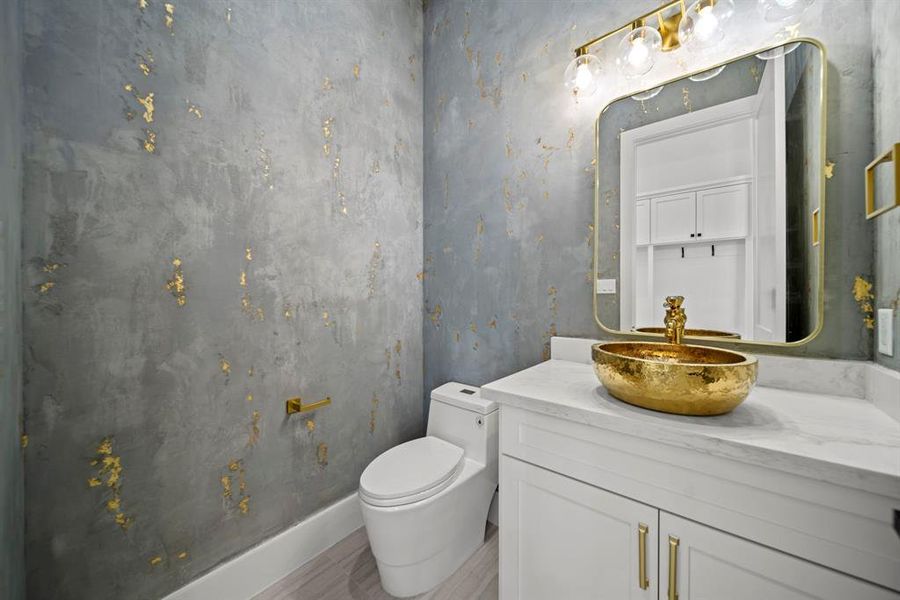 This luxurious half bath on the first floor is a statement of elegance and sophistication. Featuring a stunning gold vessel sink atop a marble countertop, it is perfectly complemented by the custom gold accents and light fixtures. The textured wall design with metallic gold detailing adds a dramatic and artistic flair, making this powder room a standout feature in the home.