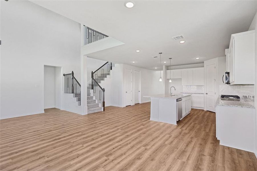 Kitchen featuring hanging light fixtures, a center island with sink, white cabinetry, stainless steel appliances, and light hardwood / wood-style floors