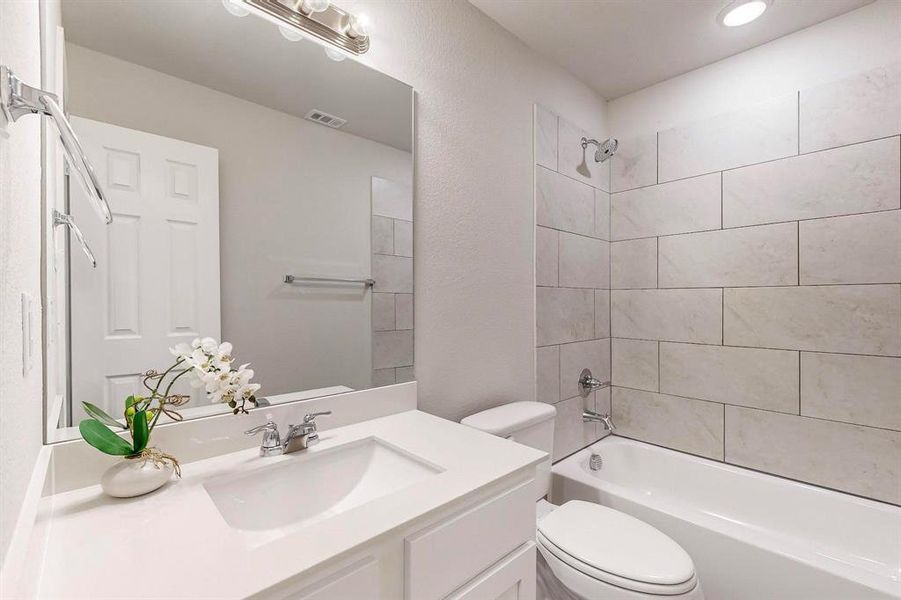 Full bathroom featuring tiled shower / bath combo, vanity, and toilet