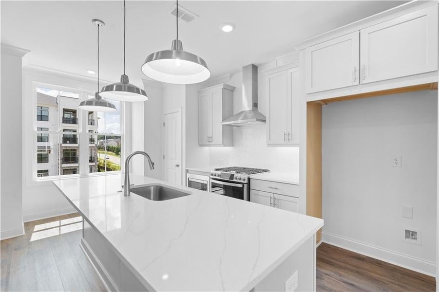 Kitchen featuring tasteful backsplash, wall chimney range hood, light stone countertops, a center island with sink, and pendant lighting Kitchen featuring tasteful backsplash, wall chimney range hood, light stone countertops, a center island with sink, and pendant lighting