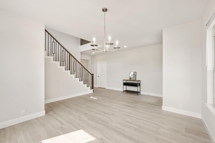 Open living area with light wood floors, staircase with metal balusters, and chandelier overhead