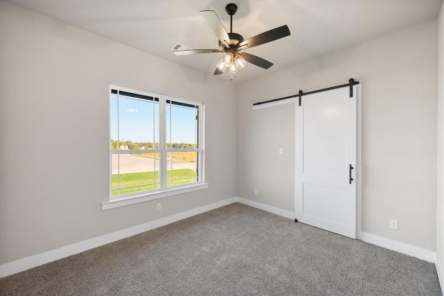 Unfurnished bedroom with ceiling fan, carpet flooring, and a barn door