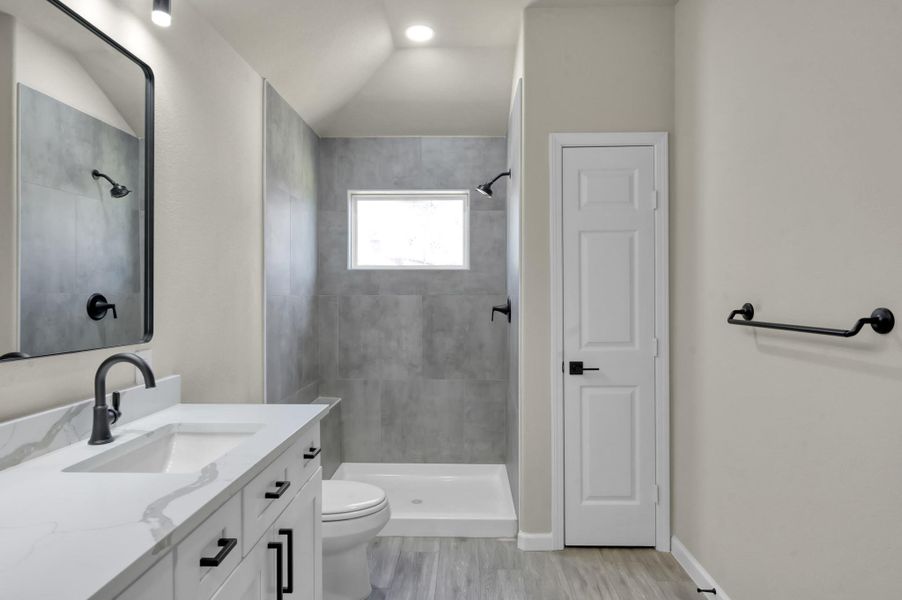 The primary ensuite offers a seamless blend of style and function, showcasing a spacious walk-in shower with floor-to-ceiling slate gray tiling, a crisp white basin, and high-contrast matte black fixtures.