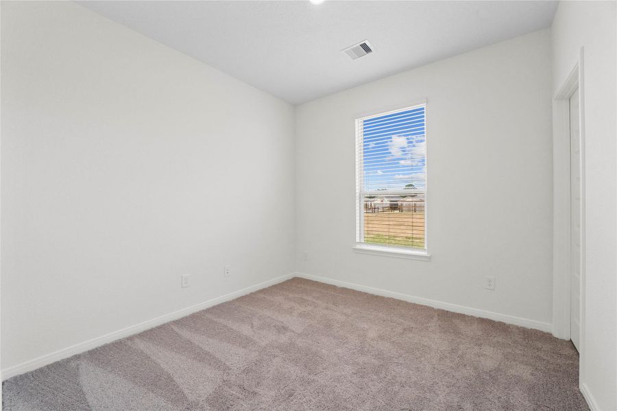 One of the three secondary bedrooms, pictured here, offers comfort and style with plush carpeting, neutral paint tones, recessed lighting, a large window with blinds, and a walk-in closet.